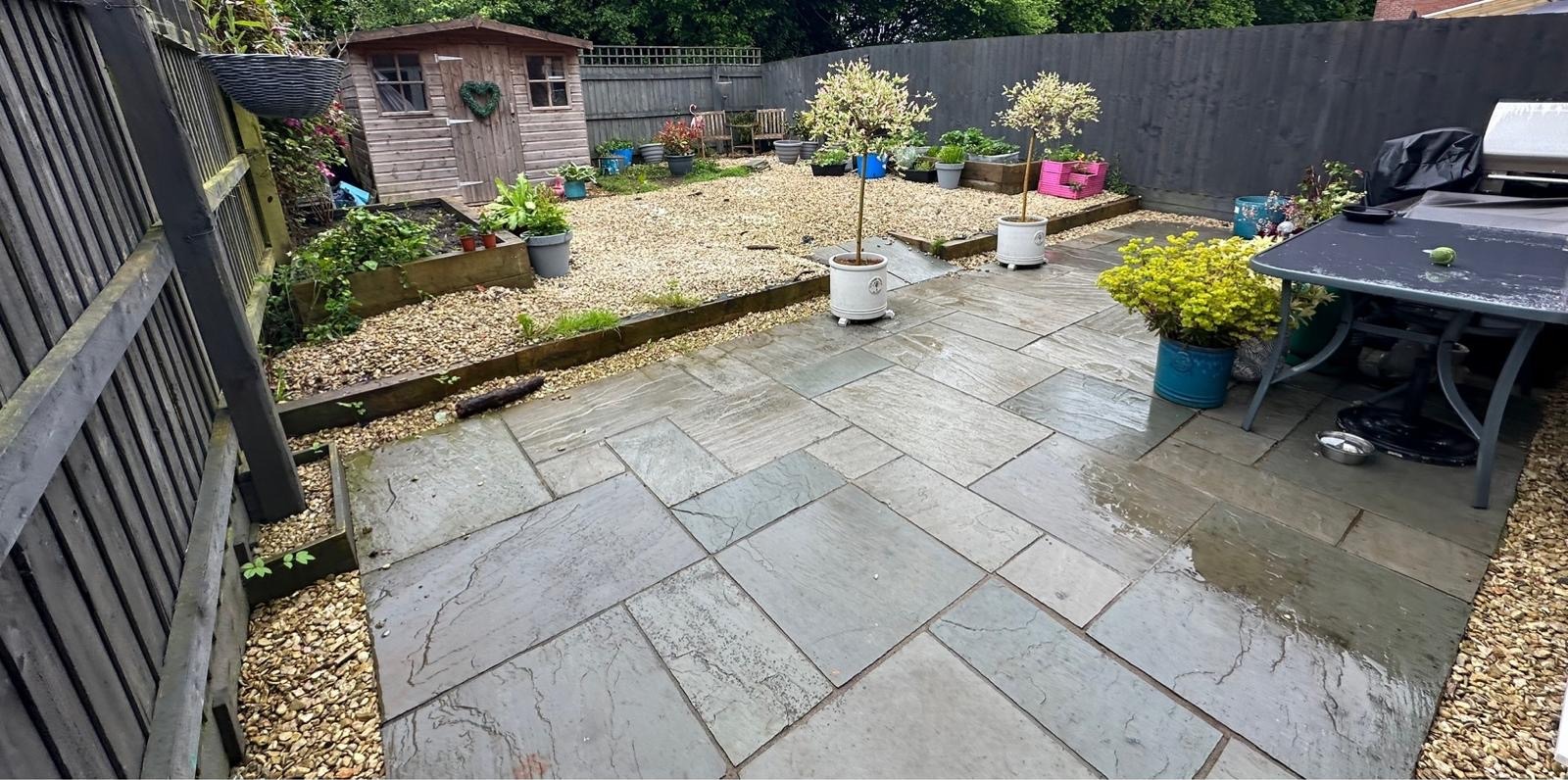 A new grey sandstone patio with gravel borders and sleeper raised beds
