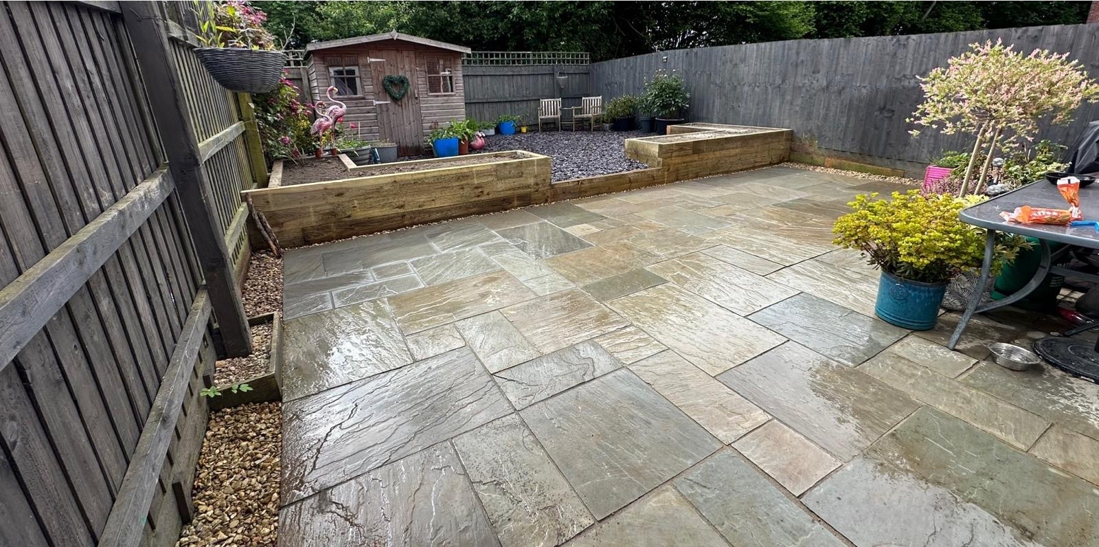 A finished sandstone patio with sleeper beds, potted trees and a summerhouse